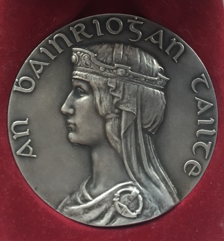 1932 Tailteann Games silver medal for rowing. The ancient Celtic Irish Queen Tailte is shown complete with Her Irish cloak, headdress and Tara brooch clasp. Dia. 50mm – hallmarked Dublin 1932. The reverse is inscribed ‘Anoch Tailteann, Baile Atha Cliath. Second Prize, Rowing; it is decorated with the four provincial crests surrounding the border. ‘Balie Atha Cliath’ translates as ‘Dublin City’ where most of the events were held but the rowing events took place there only once, in 1924. In 1928, they were held in Cork and in 1932 in Drogheda.