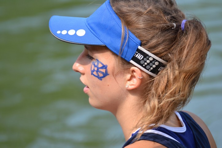 Pic 24. A member of St Catherine’s Boat Club waiting for Women’s Division II. She displays the ‘Catherine Wheel’ in both her face paint and her earring. St Catherine, a Fourth Century martyr, was to be tortured on a spiked breaking wheel but it shattered on her touch. The college claims to be the only one with a torture device as a symbol.