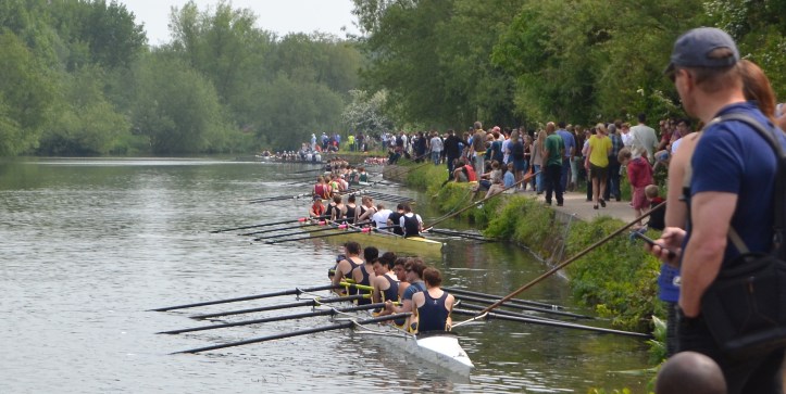 To make sure that the boats start the same distance apart and at the same time, the cox must hold a rope 50 feet in length fastened to a post. The posts are 130 feet apart. When the one minute cannon is fired, boatman push their crew out with a long pole and the cox takes the strain on the rope. Here, Men’s Division IV relaxes before all this happens.