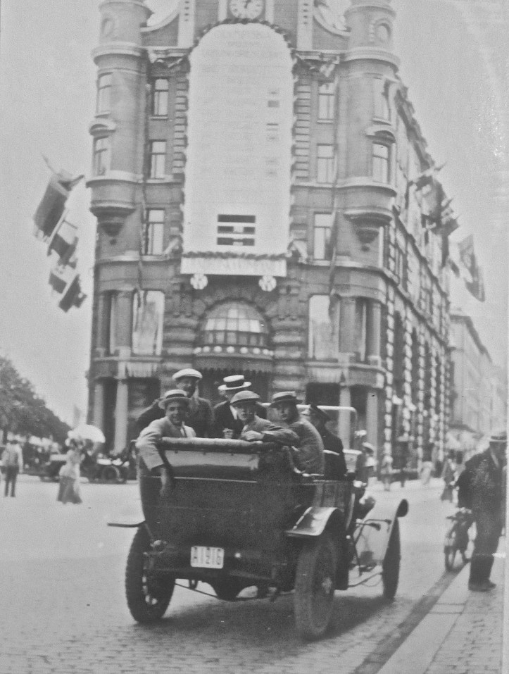 A car full of celebrating Leander men is parked under a rowing results board which was affixed to the department store, Nordiska Kompaniet (‘The Nordic Company’).